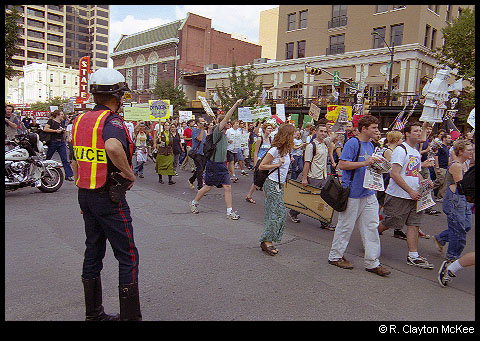 An Austin Police Officer watches protesters march down Congress Avenue during the Fortune 500 meeting protest.